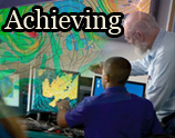 3 Two meteorologists analyze weather data on computer screens with a large weather map behind them. The image contains the text "Achieving".