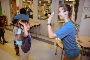 Mental Health 2 A teacher high-fives a young student in a classroom line.