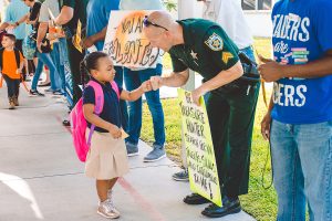SAFE 1 A young girl in a school uniform fist-bumps a police officer holding a sign that reads "Be a Treasure Hunter, Search for what's talents, skills and intelligence lie." Other adults hold signs nearby.