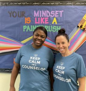 School_counselors Two smiling school counselors stand in front of a bulletin board that reads "Your Mindset Is Like A Paintbrush." They wear matching blue t-shirts that say "Keep Calm I'm A Counselor.